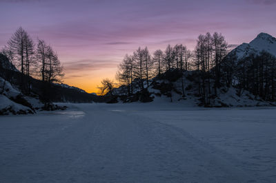 Snow covered field against sky during sunset