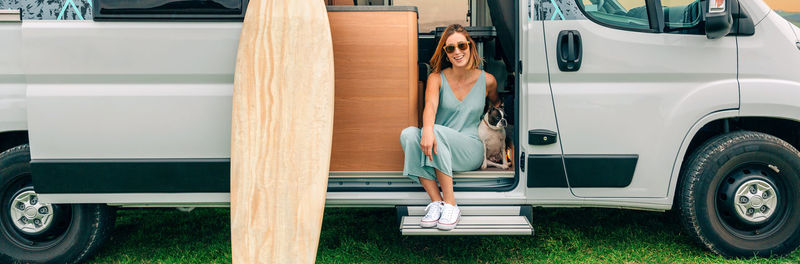 Woman sitting with her dog at the door of her camper van during a trip