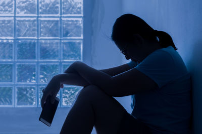 Silhouette depress woman sitting and hold smartphone in hand.