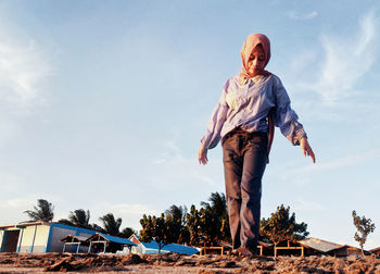 A girl is standing on the beach against the background of buildings, trees, clouds and sky