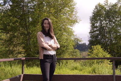 Portrait of young woman standing by railing against trees