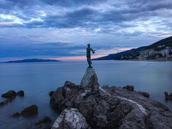 Man standing on rock by sea against sky