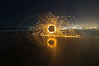 Man standing amidst illuminated wire wool by sea at night