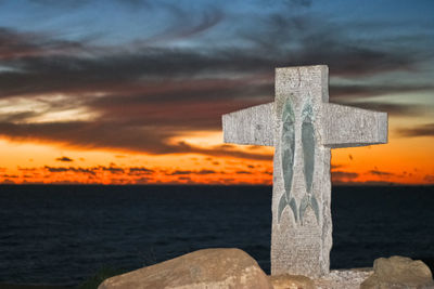 Close-up of cross against sea during sunset
