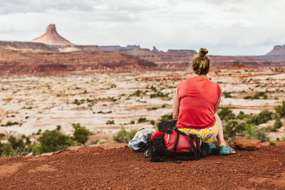 Sweaty female sits on backpack during a hiking break at desert view