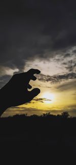 Silhouette person hand against sky during sunset