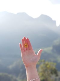 Cropped hand of woman holding yellow flower against mountains