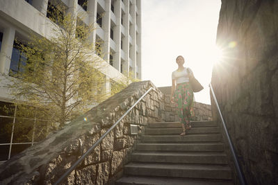 Low angle view of woman moving down on steps against sky during sunny day