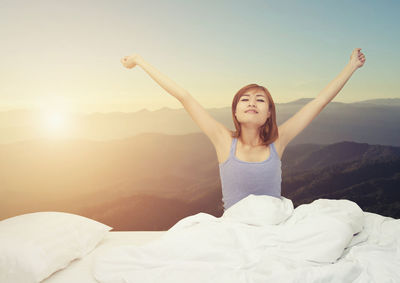 Woman stretching hands on bed against mountains