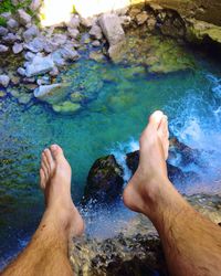 Low section of man sitting on rock at waterfall