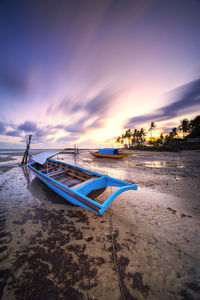 Boat moored on beach against sky during sunset