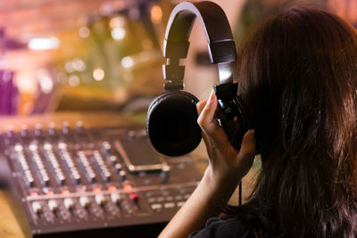 Rear view of woman holding headphone while standing by audio equipment