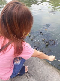 High angle view of girl crouching by water while holding stick