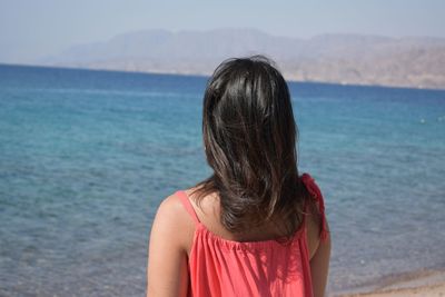Rear view of woman standing at beach on sunny day