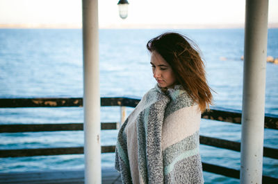 Thoughtful young woman standing on pier over sea