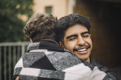 Happy boy with eyes closed embracing male friend