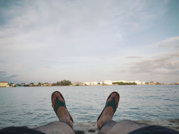 Low section of person relaxing by sea against sky