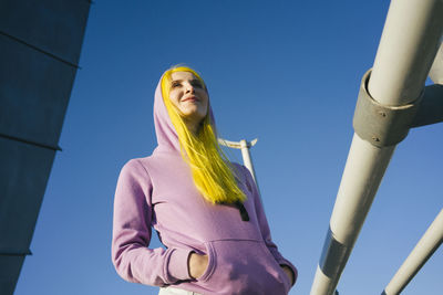 Low angle view of woman looking away against clear blue sky