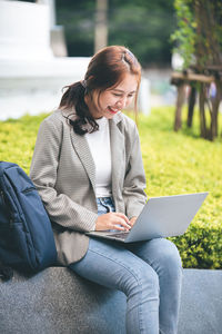 Young woman using laptop while sitting outdoors