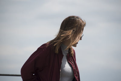 Young woman looking away while standing against sky