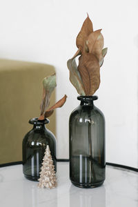 Dried leaves in black glass vases stand on the table and a decorative christmas tree