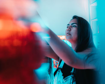 Young woman looking away while standing against illuminated wall