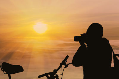 Silhouette man photographing against sky during sunset