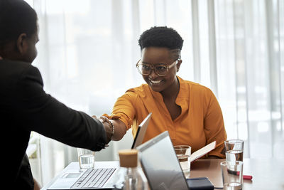 Smiling businesswoman shaking hand with male coworker at office