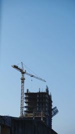 Low angle view of crane by building against clear sky