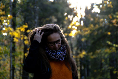 Young woman looking down while standing against trees