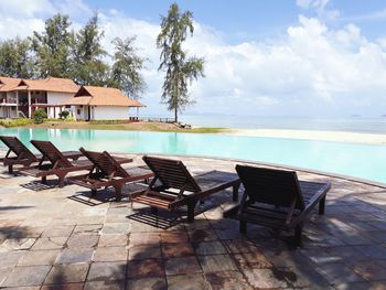 Chairs on beach by swimming pool against sky