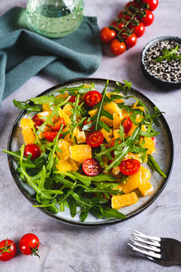 Dietary salad of orange slices, cherry tomatoes and arugula on a plate on the table vertical view