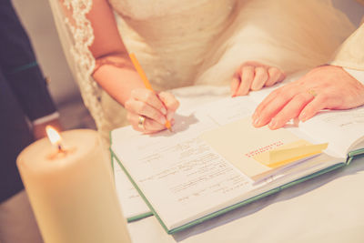 Midsection of bride signing in paper at table