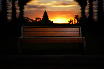 Empty bench by silhouette trees against sky during sunset