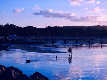 Silhouette people walking in lake against sky during sunset