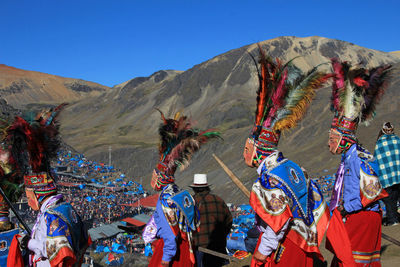 People in traditional clothing dancing on sand against mountains and sky