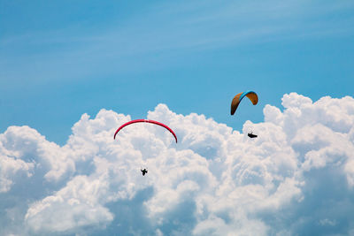 Low angle view of people paragliding against sky