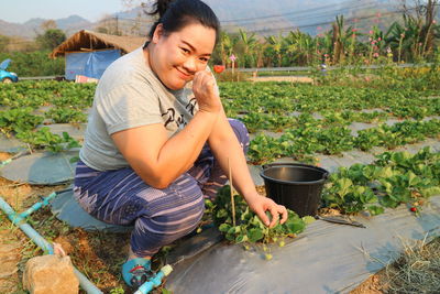 Portrait of smiling woman harvesting strawberry on farm