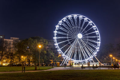 Ferris wheel in illuminated city against sky at night