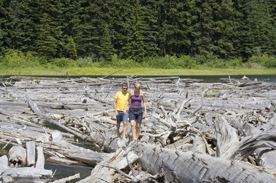 Man and woman walking amidst driftwoods at duffey lake provincial park