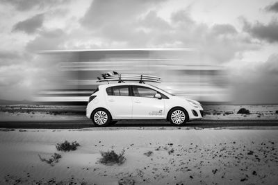 Blurred motion of truck by car on road against cloudy sky