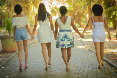 Rear view of women holding hands while walking on footpath