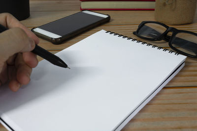 Cropped hand of woman using mobile phone on table