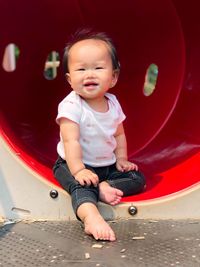 Full length of smiling cute girl sitting on equipment in playground