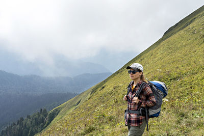 Young woman hiker in cap sunglasses with hiking backpack looking at mountain view of aibga ridge 