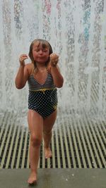 Full length of wet girl in swimsuit walking by fountain