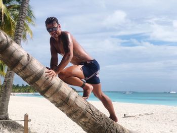 Full length of shirtless man at beach against sky