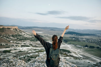 Rear view of woman sitting on mountain against sky during sunset