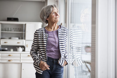 Portrait of senior woman looking through window at home