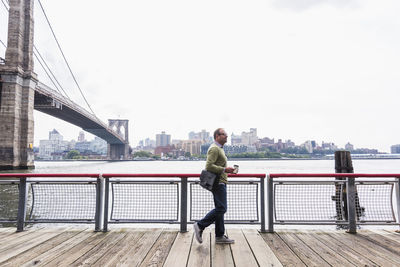 Man on bridge over river against sky in city